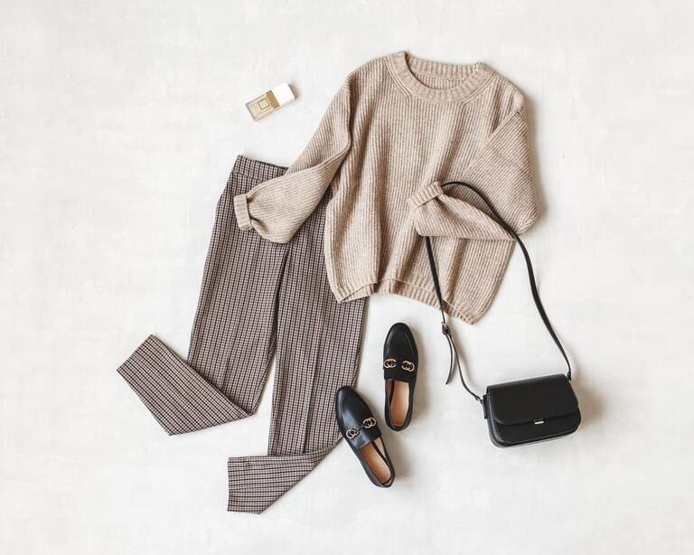 Brown pants in check, beige knit sweater, crossbody bag, black loafers or flat shoes on gray background. Overhead view of women's casual day dress. Lie flat, top view. Women's clothing.